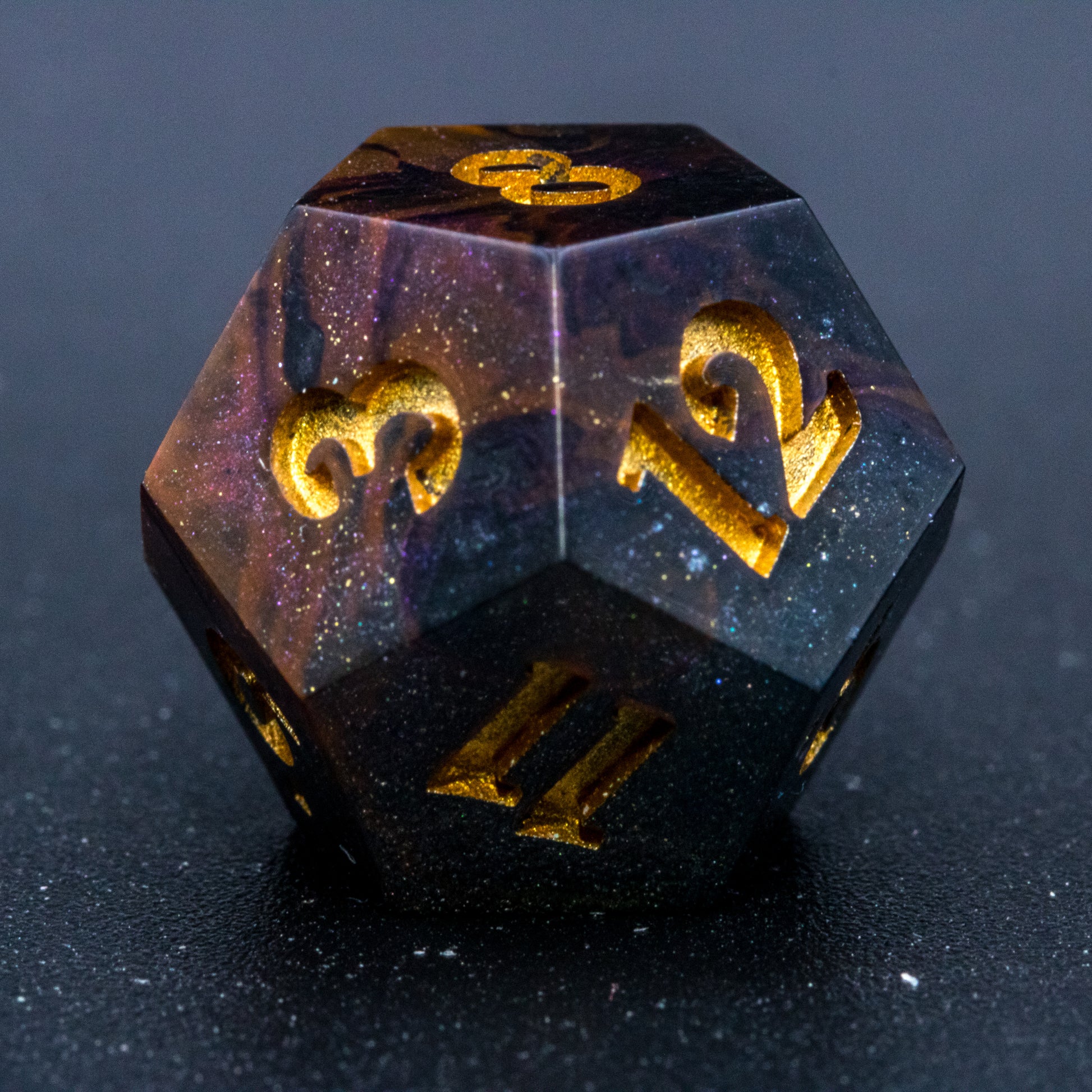 Close up of Astral Glory D12 die, featuring galaxy-like colouring of deep orange and purple swirls over black and deep blue with golden starry specks. Numbers are painted a deep gold.