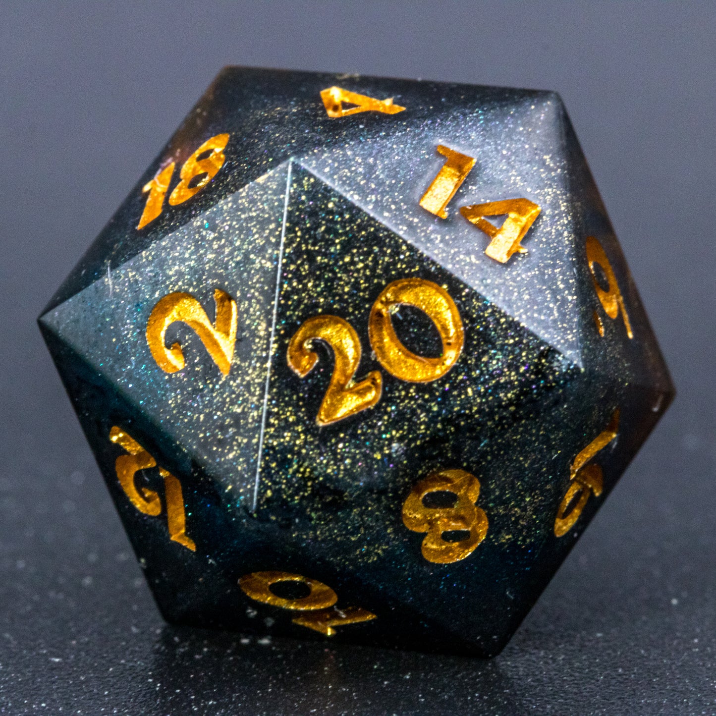 Close up of Astral Glory D20 die, featuring galaxy-like colouring of deep orange and purple swirls over black and deep blue with golden starry specks. Numbers are painted a deep gold.