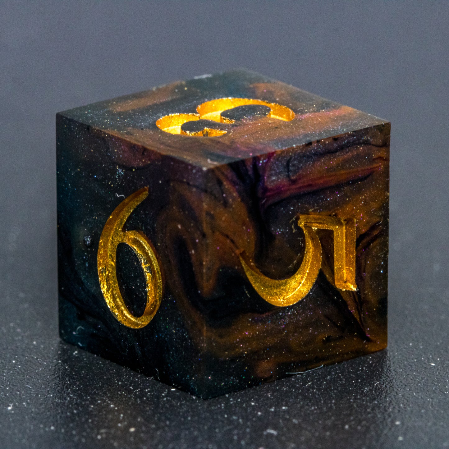 Close up of Astral Glory D6 die, featuring galaxy-like colouring of deep orange and purple swirls over black and deep blue with golden starry specks. Numbers are painted a deep gold.