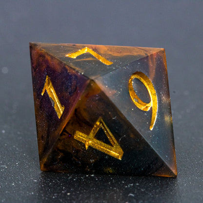 Close up of Astral Glory D8 die, featuring galaxy-like colouring of deep orange and purple swirls over black and deep blue with golden starry specks. Numbers are painted a deep gold.