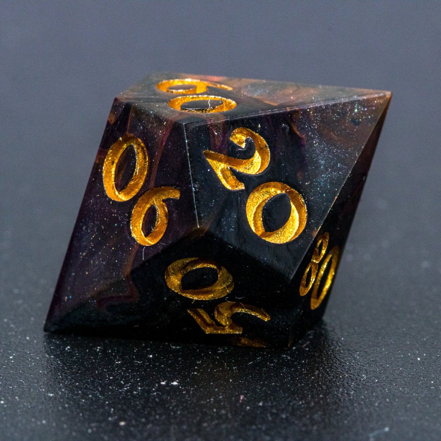 Close up of Astral Glory D% die, featuring galaxy-like colouring of deep orange and purple swirls over black and deep blue with golden starry specks. Numbers are painted a deep gold.