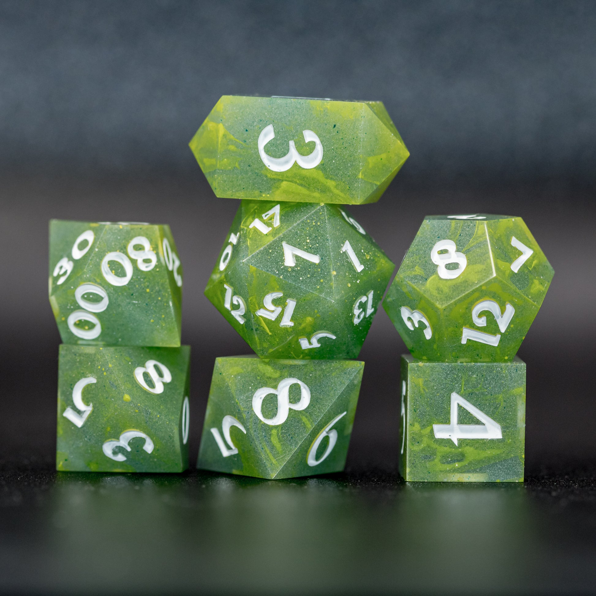 Stacked front view of all Bog Brew dice using flash, featuring white numbers, yellow-green swirls on blue-green base resin.