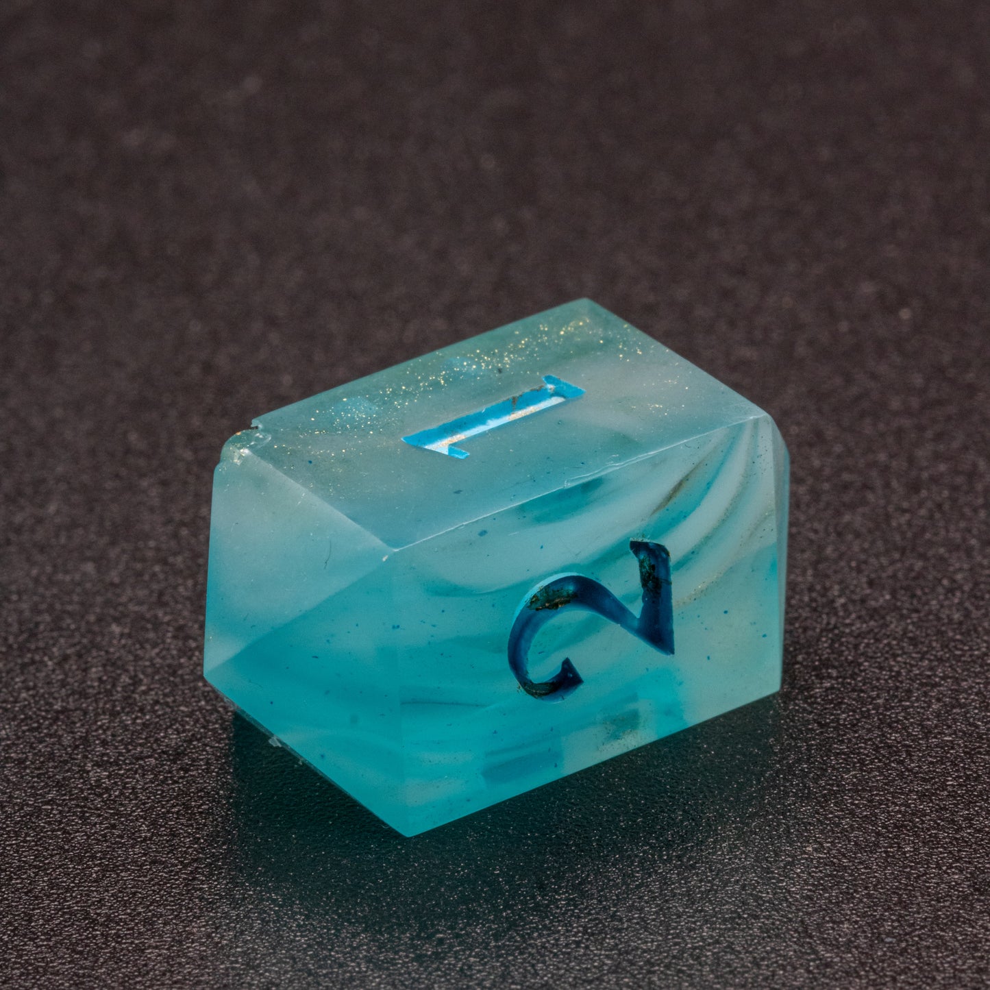 Zoomed in photo of a wavy blue-white and speckled gold D4 crystal die with an slight bubble on one corner.