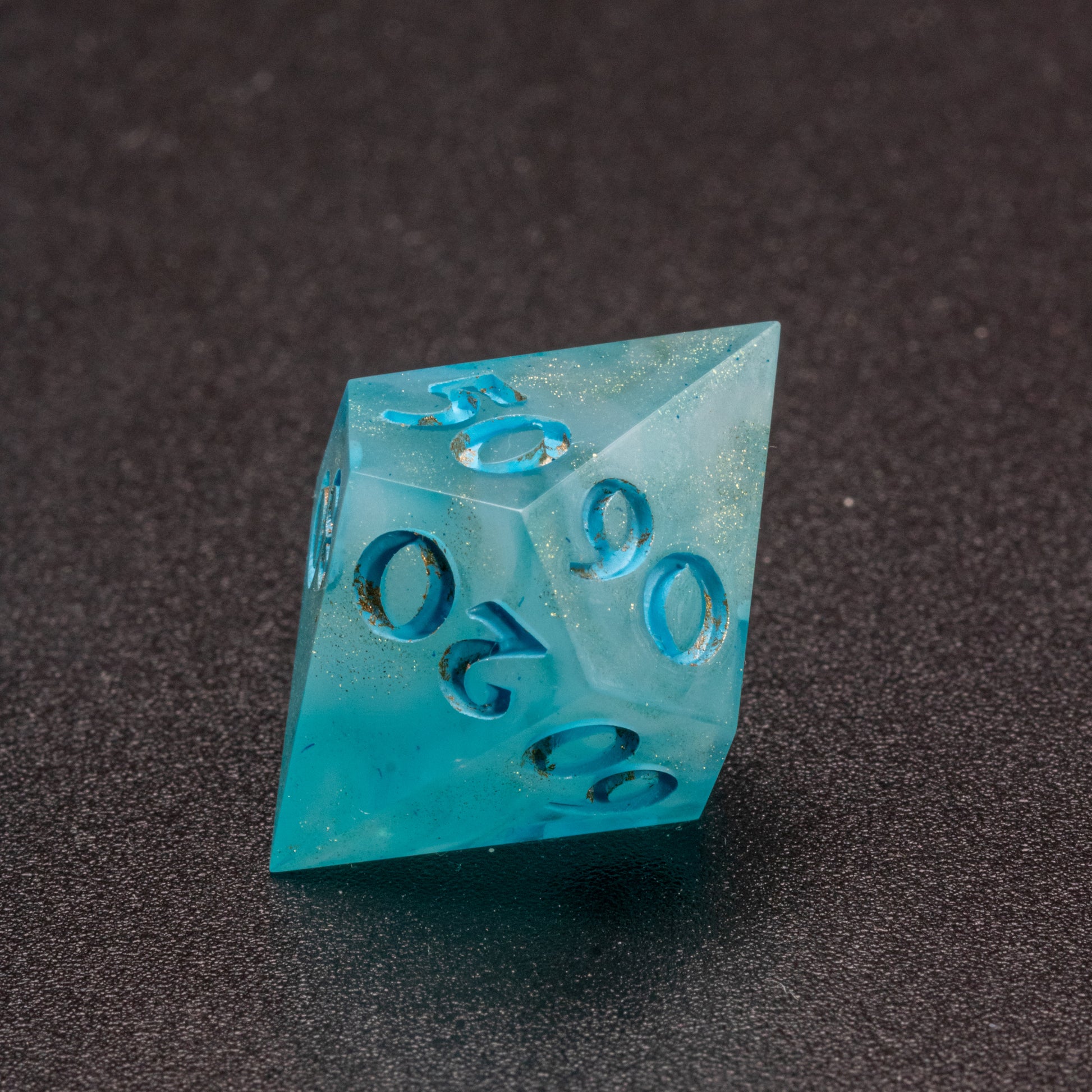 Zoomed in photo of a wavy blue-white and speckled gold D% (10-sided) die.