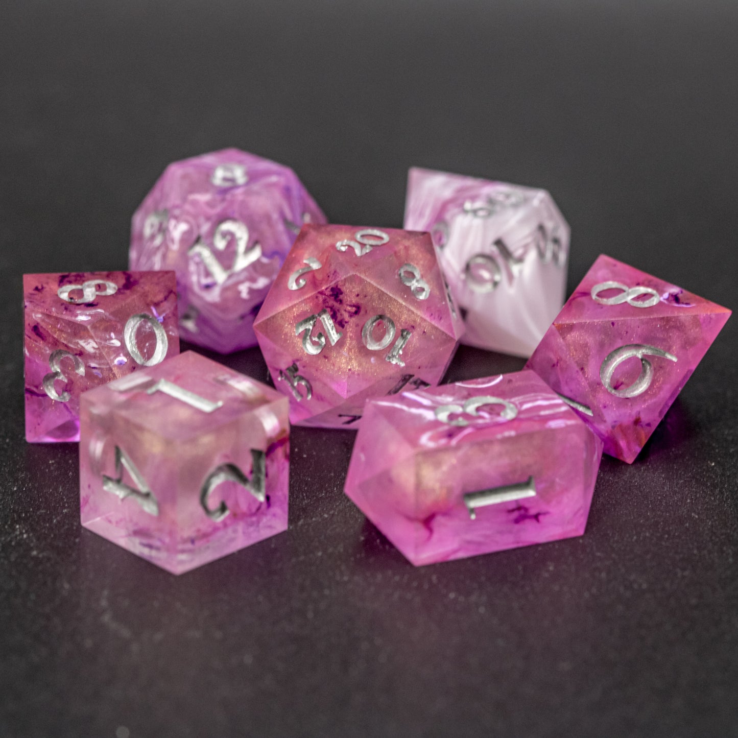 Soul Crystal Dice Set arranged in a circle with central D20, featuring purple and pink swirls over a pink translucent base with sparkly gold, and silver-painted numbers.