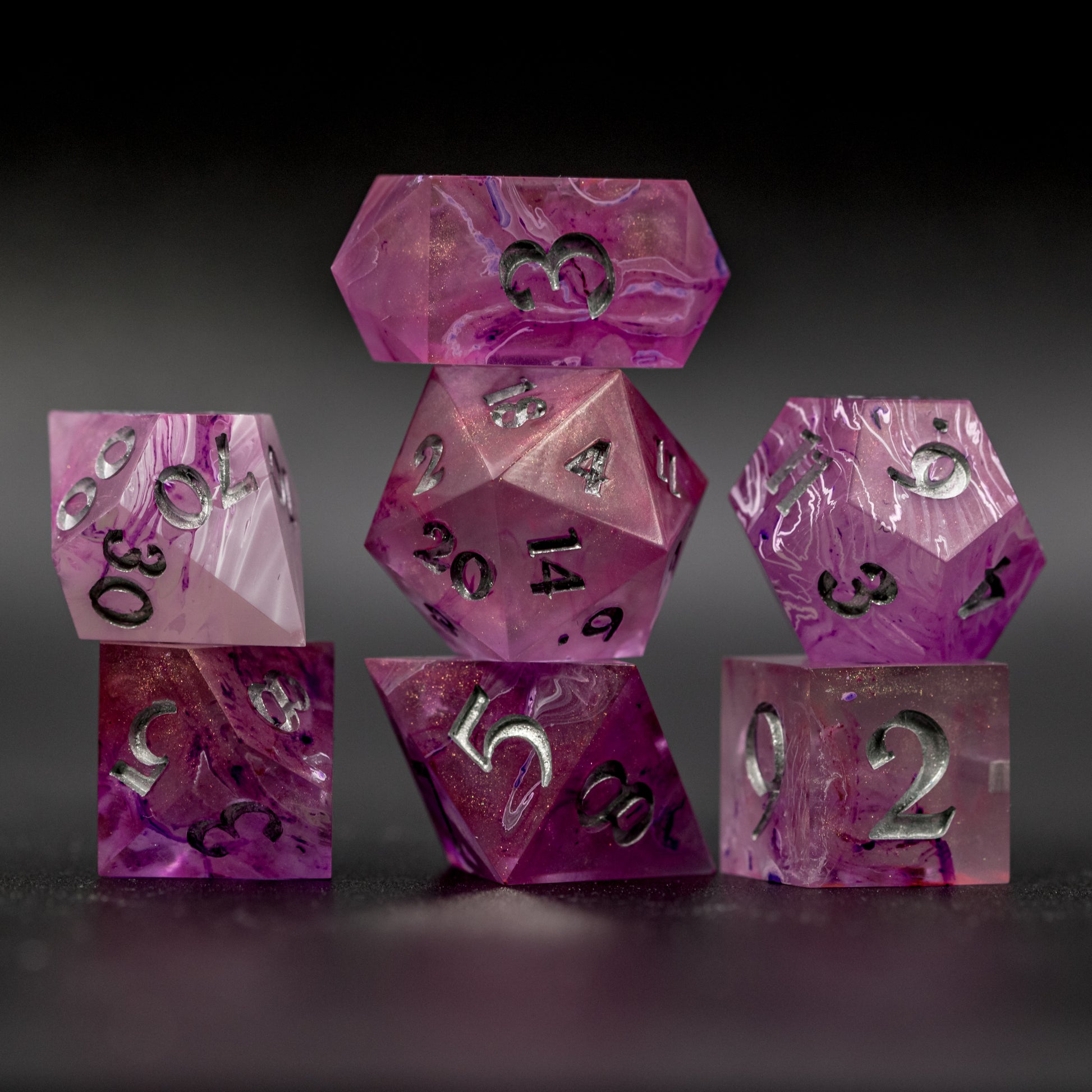 Stacked front view of Soul Crystal Dice Set, featuring purple and pink swirls over a pink translucent base with sparkly gold, and silver-painted numbers.