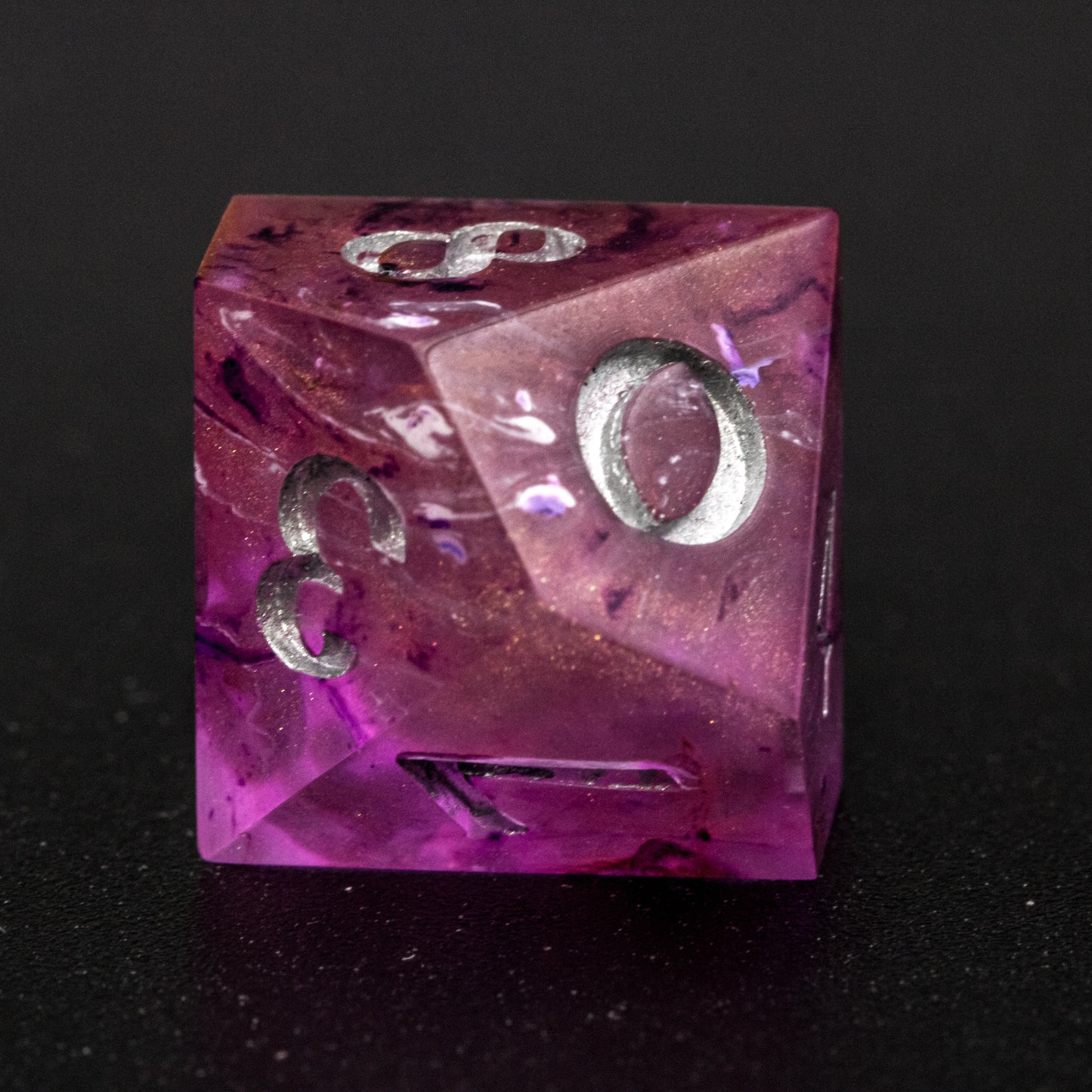 Close up of Soul Crystal D10 die, featuring purple and pink swirls over a pink translucent base with sparkly gold, and silver-painted numbers.