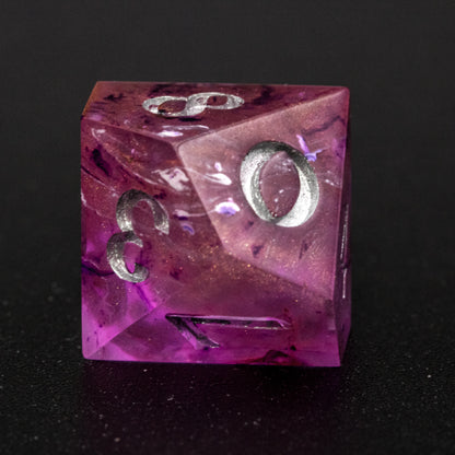 Close up of Soul Crystal D10 die, featuring purple and pink swirls over a pink translucent base with sparkly gold, and silver-painted numbers.