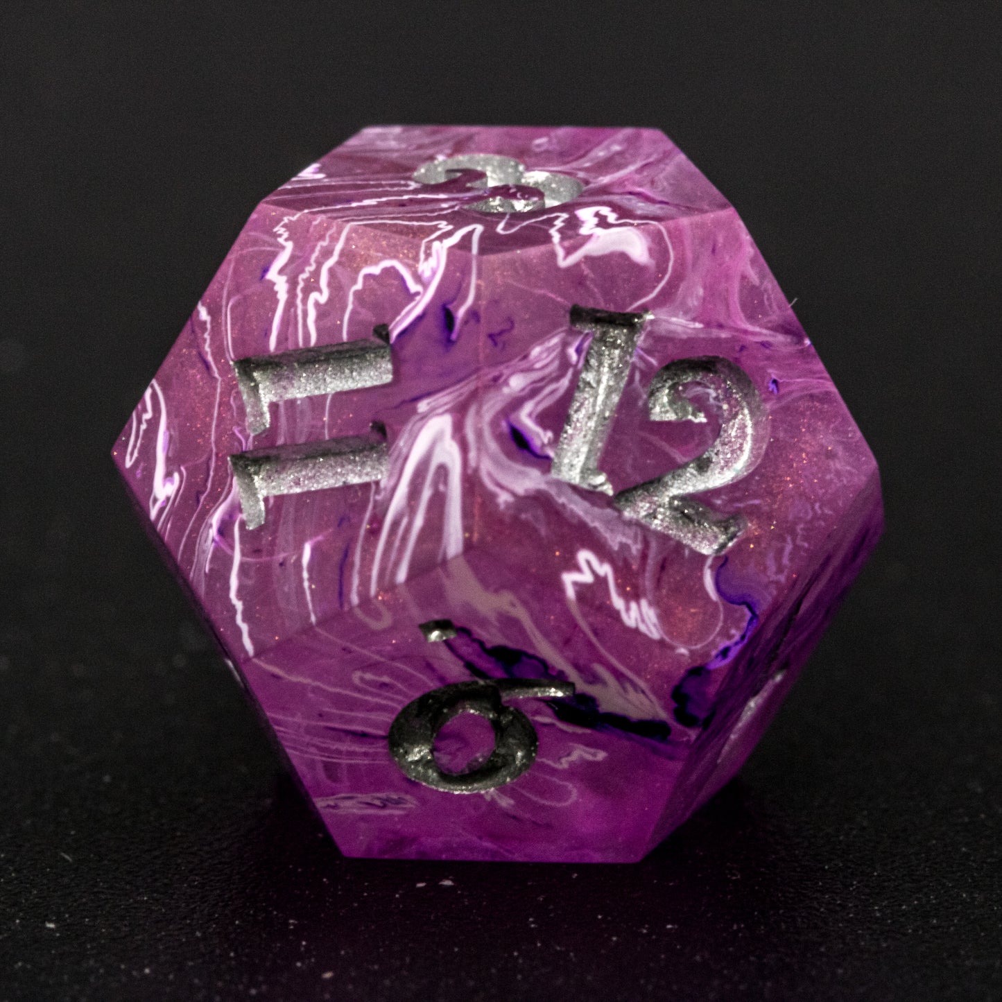 Close up of Soul Crystal D12 die, featuring purple and pink swirls over a pink translucent base with sparkly gold, and silver-painted numbers.