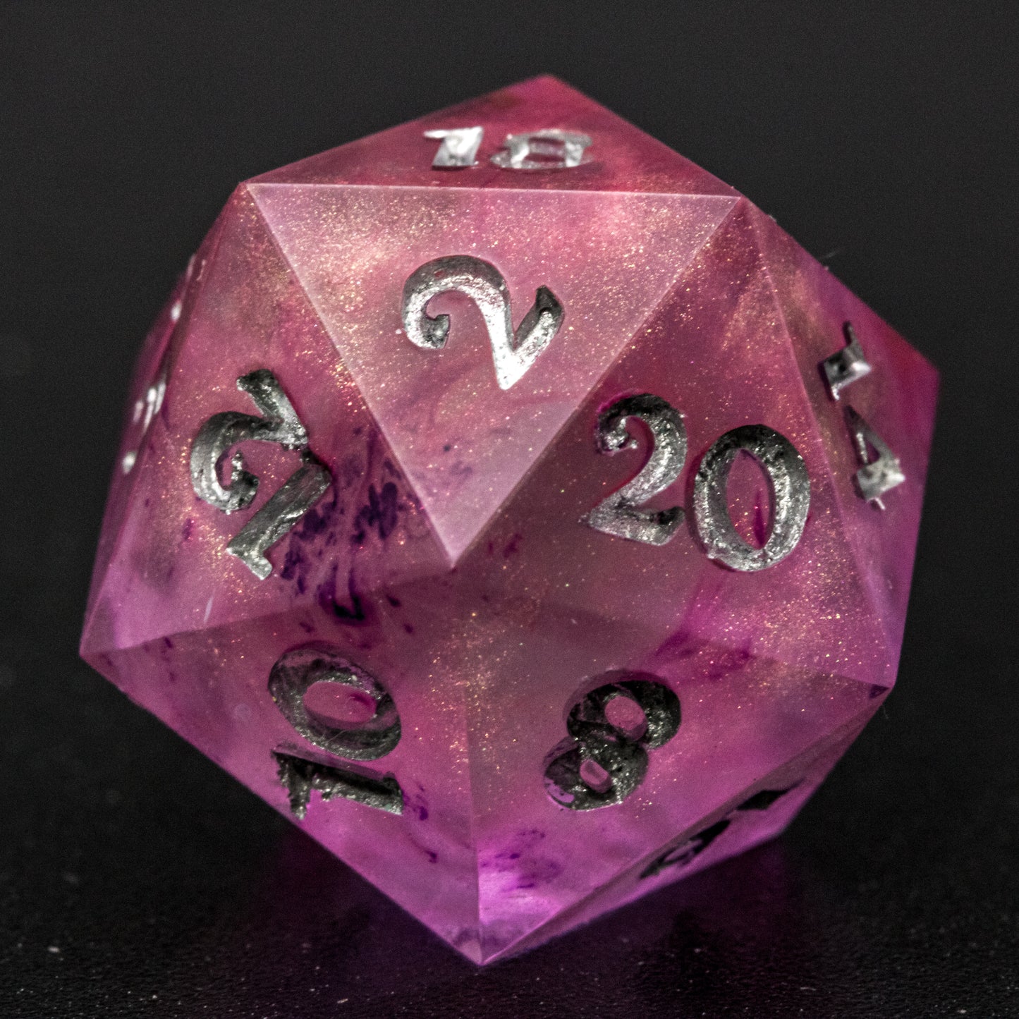 Close up of Soul Crystal D20 die, featuring purple and pink swirls over a pink translucent base with sparkly gold, and silver-painted numbers.