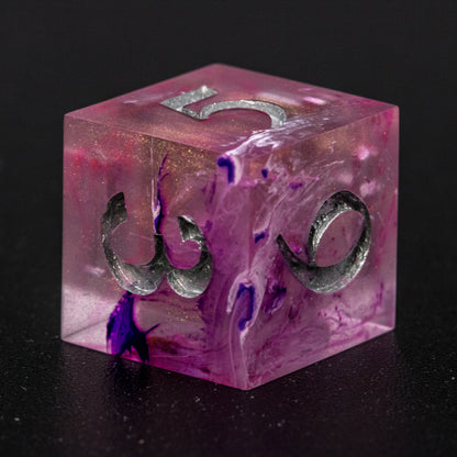 Close up of Soul Crystal D6 die, featuring purple and pink swirls over a pink translucent base with sparkly gold, and silver-painted numbers.