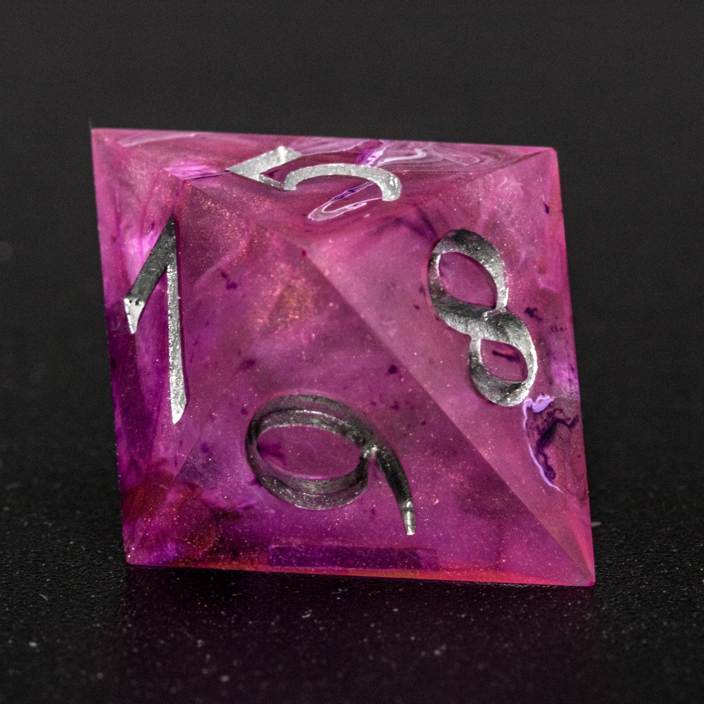 Close up of Soul Crystal D8 die, featuring purple and pink swirls over a pink translucent base with sparkly gold, and silver-painted numbers.