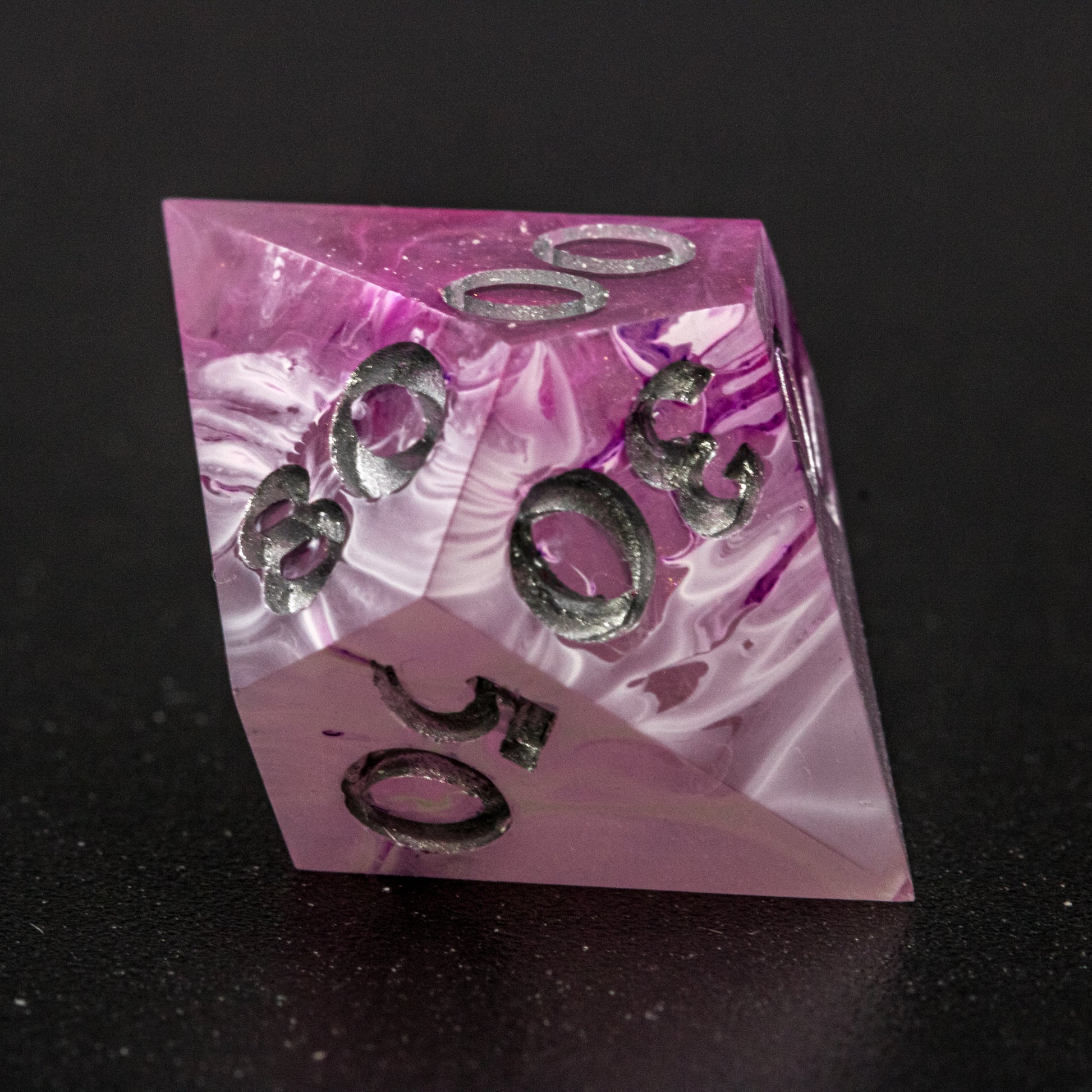 Close up of Soul Crystal D% die, featuring purple and pink swirls over a pink translucent base with sparkly gold, and silver-painted numbers.